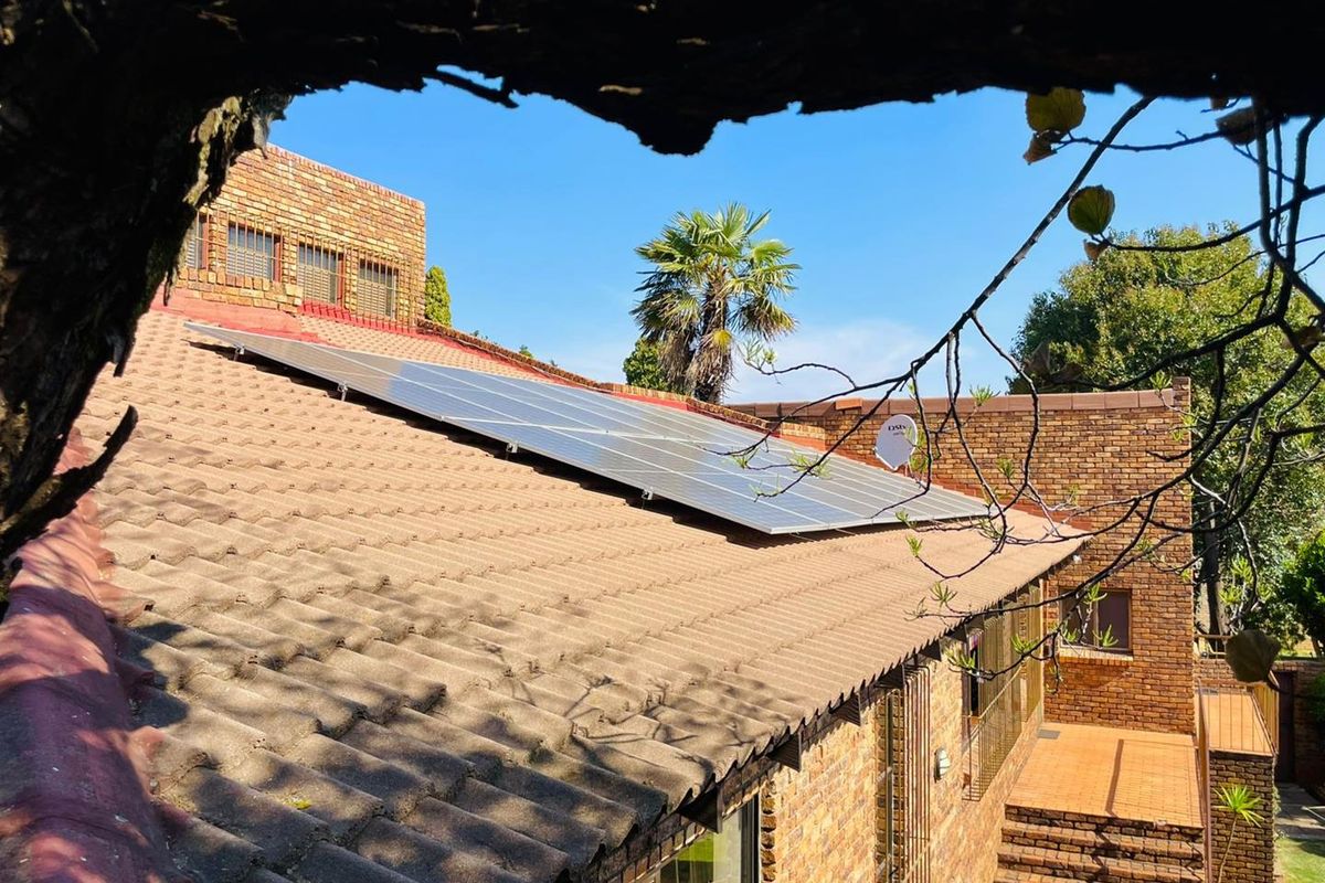 Rear view of the property featuring a facebrick facade, tiled roof with installed solar panels, and a brick staircase leading to the garden area.