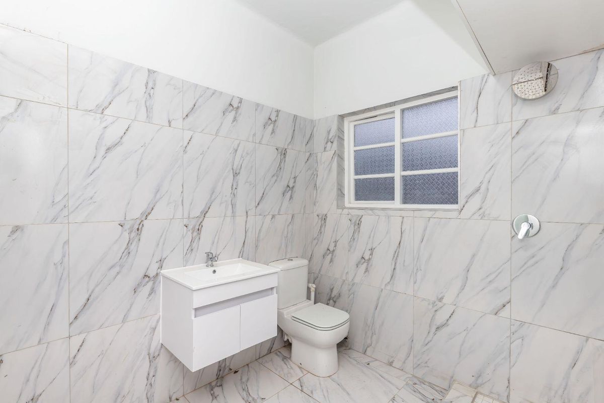 A clean, modern bathroom featuring marble-look wall tiles, a wall-mounted vanity, and a functional shower setup with an obscured glass window.