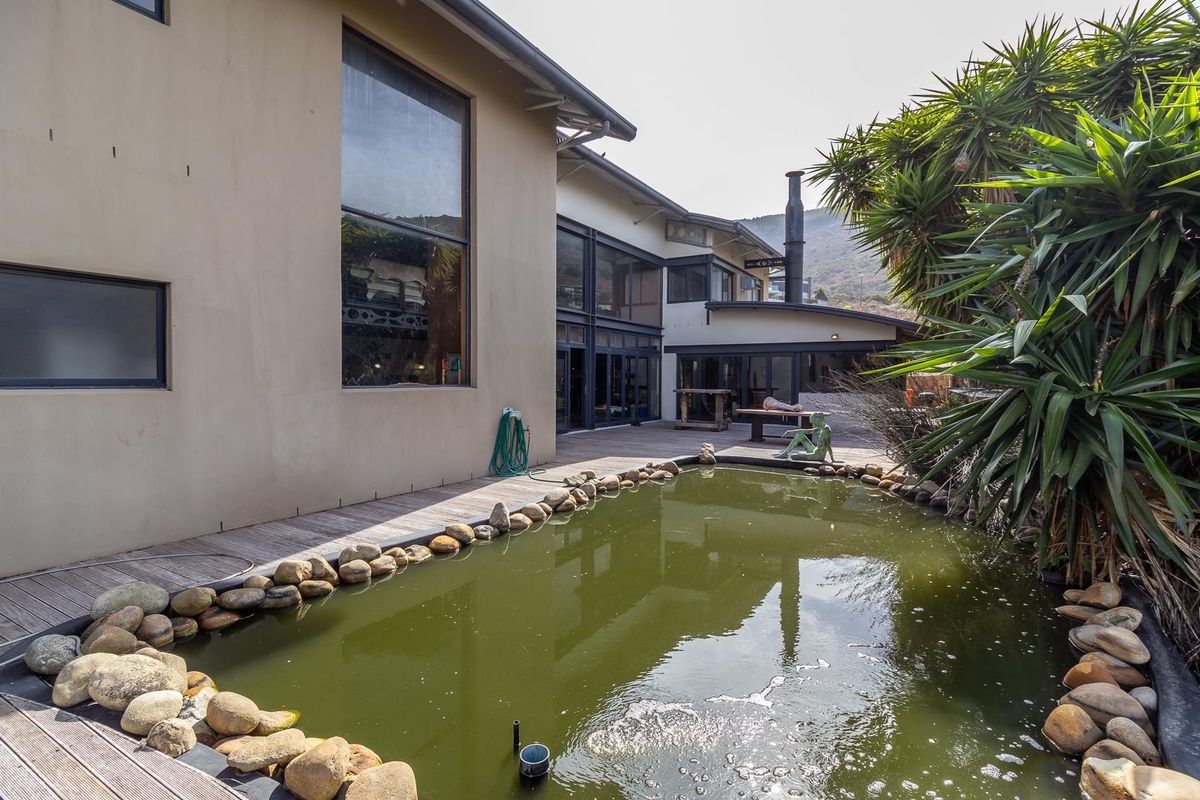 Rear exterior view featuring a timber deck, a stone-bordered pond, and large glass windows overlooking the garden area.