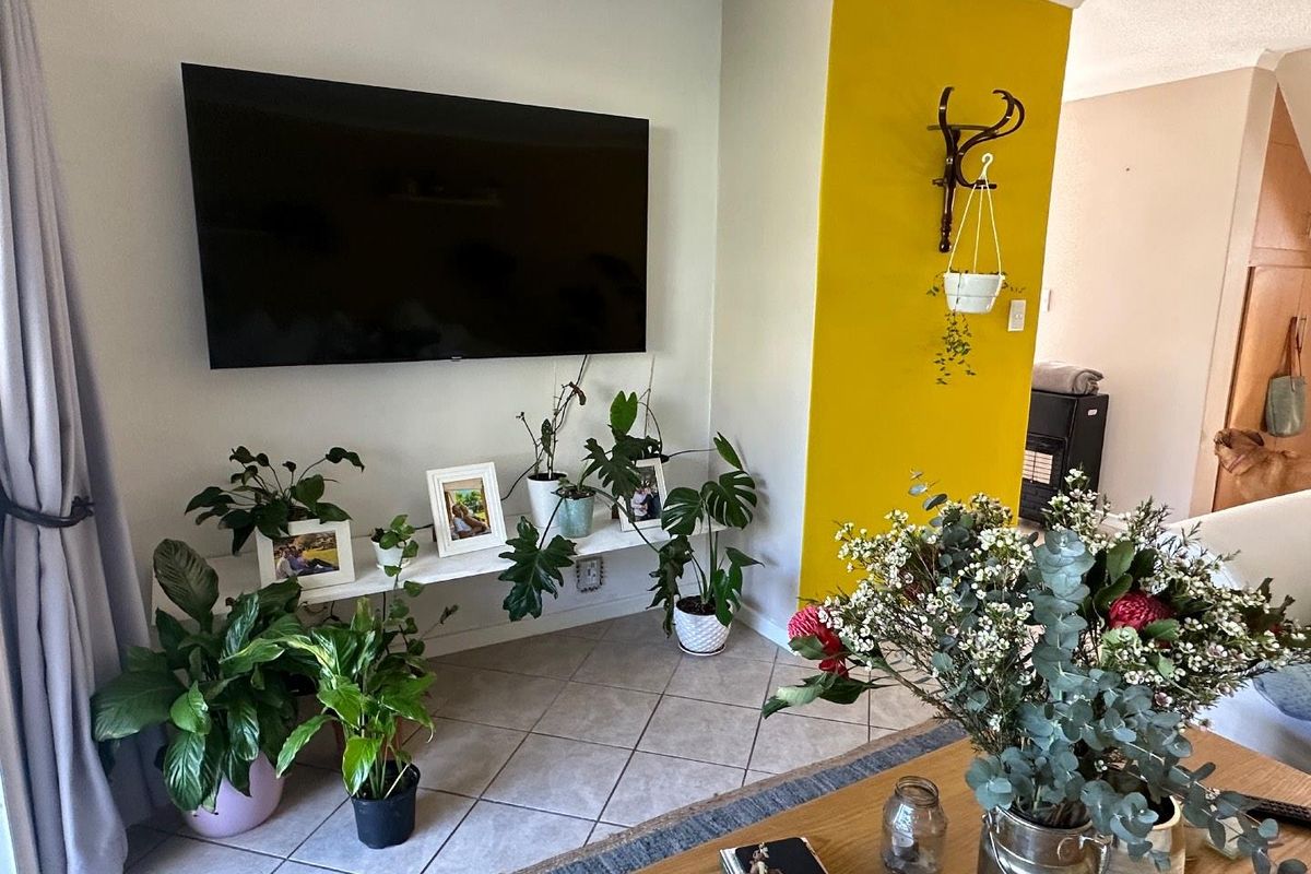 A living room area featuring tiled flooring, a wall-mounted television, and a distinctive yellow accent wall.