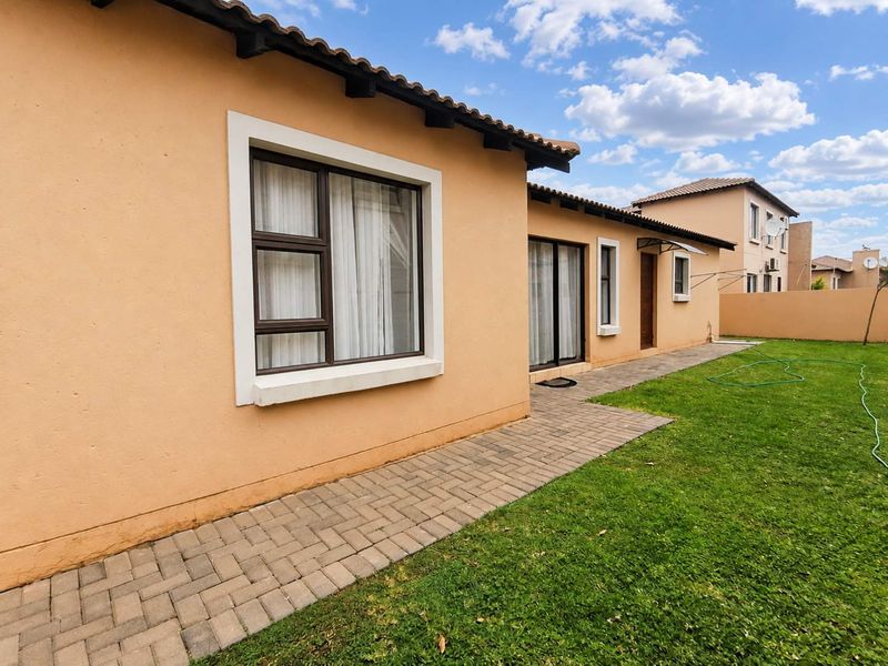 Rear view of the townhouse featuring a paved walkway, well-maintained lawn, and sliding glass doors providing access to the interior.