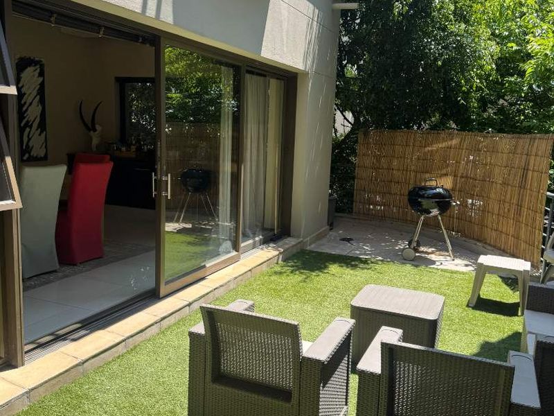 A private ground-floor patio featuring artificial turf, paved sections, and sliding glass doors providing seamless access to the interior living space.