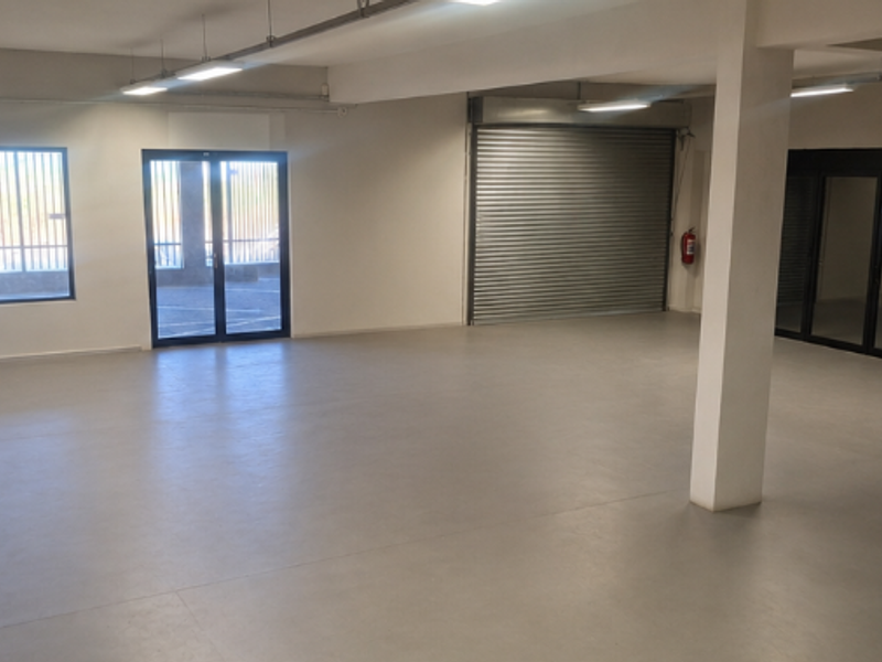 Spacious open-plan office area featuring polished concrete flooring, roller shutter access, and ample natural light through large windows and glass doors.