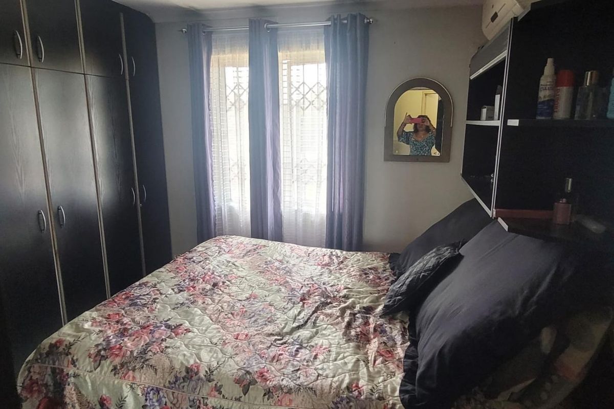 A bedroom featuring dark built-in cupboards, a wall-mounted air conditioning unit, and a window fitted with a security gate.