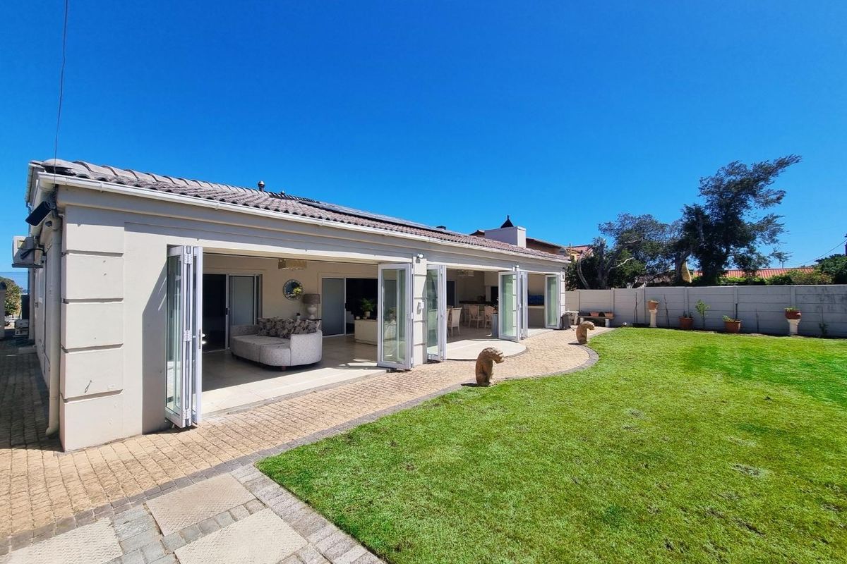 Spacious rear exterior view featuring a large manicured lawn, paved patio area, and wide-opening bi-fold doors leading into the open-plan living space.