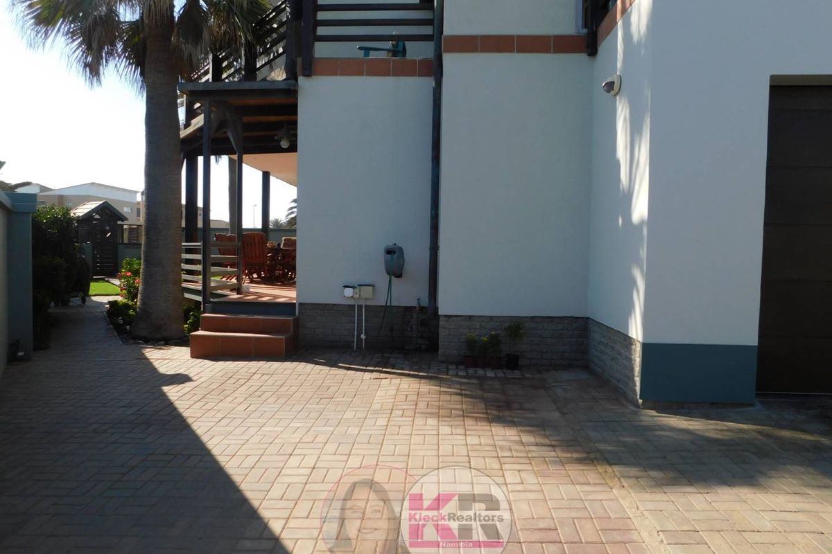 A paved driveway area leading to a covered patio and garage, featuring a palm tree and exterior wall finishes.