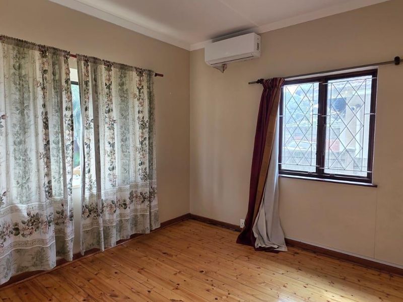 A bright, empty bedroom featuring polished timber flooring, a wall-mounted split-system air conditioner, and windows fitted with security bars.