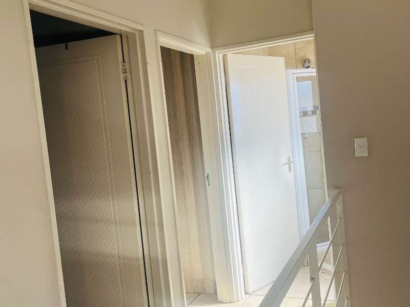 A bright, tiled hallway featuring a metal balustrade and access to multiple internal rooms.
