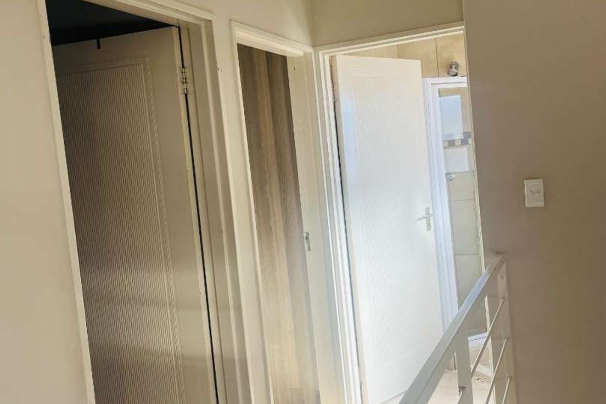 A bright, tiled hallway featuring a metal balustrade and access to multiple internal rooms.