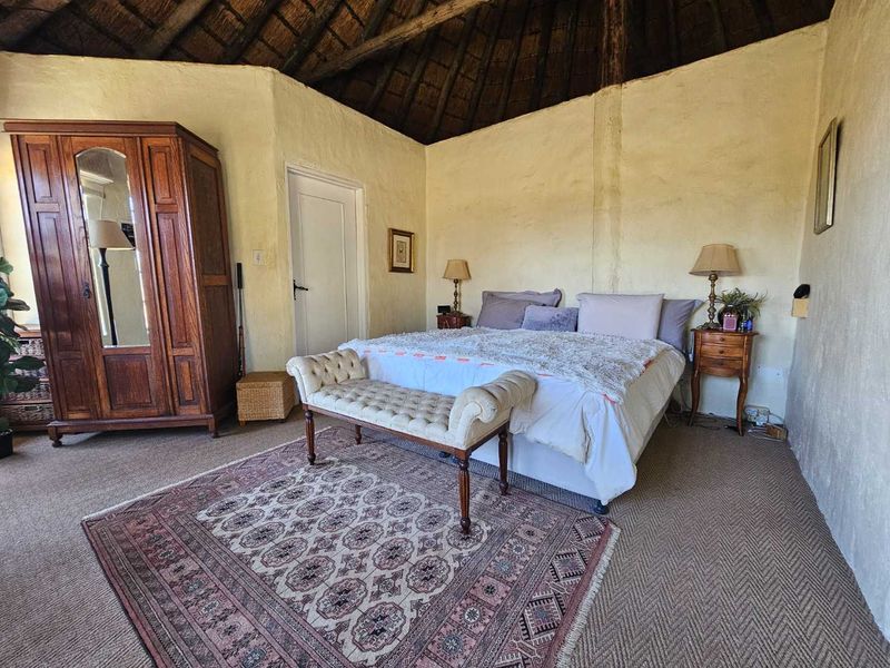 A rustic bedroom featuring a traditional thatched roof with exposed timber rafters and textured plaster walls, offering a cozy farm-style atmosphere.