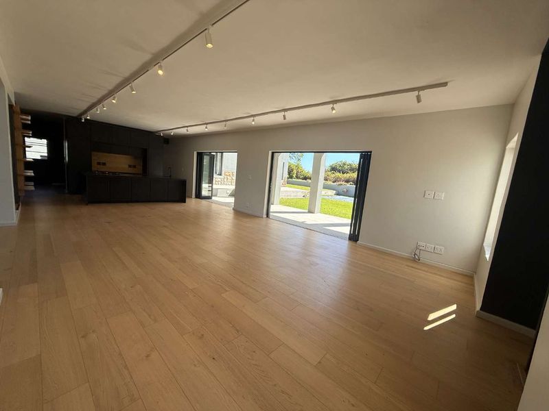Spacious open-plan living area featuring timber flooring, modern track lighting, and large bi-fold doors opening to an outdoor patio and garden.