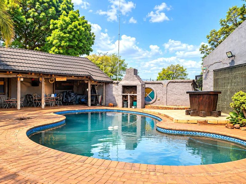 Outdoor pool area featuring a kidney-shaped swimming pool, covered patio with built-in braai, and brick-paved surround.
