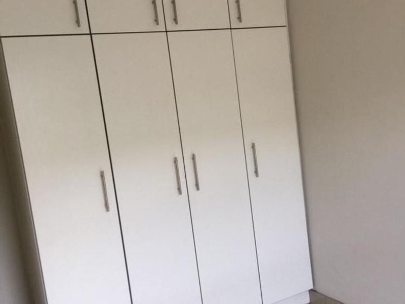 A clean bedroom featuring floor-to-ceiling white built-in cupboards and neutral tiled flooring.
