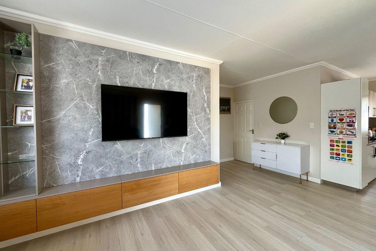 A modern living room featuring a custom built-in media unit with marble-effect paneling, wood cabinetry, and light-toned laminate flooring.
