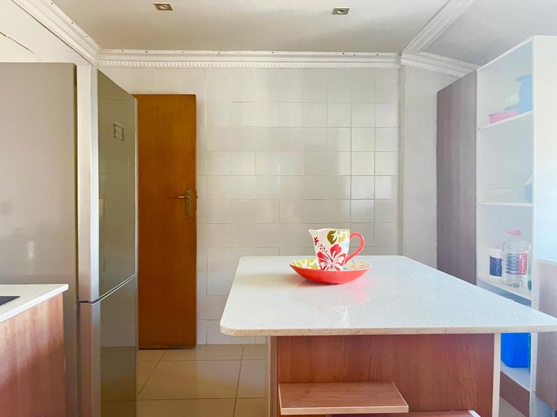 A functional kitchen area featuring a central island, tiled splashback, and built-in shelving, offering potential for a modern cosmetic update.
