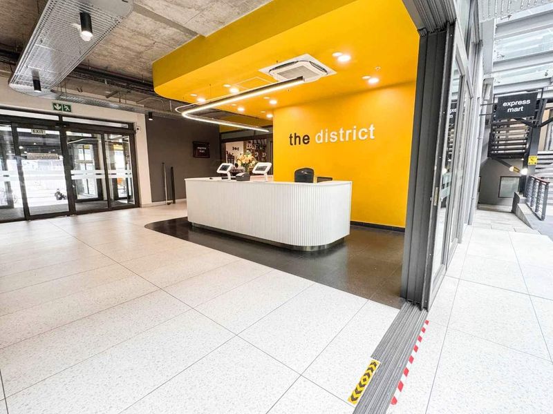Modern commercial reception area featuring a bright yellow accent wall, sleek reception desk, tiled flooring, and contemporary exposed ceiling design.