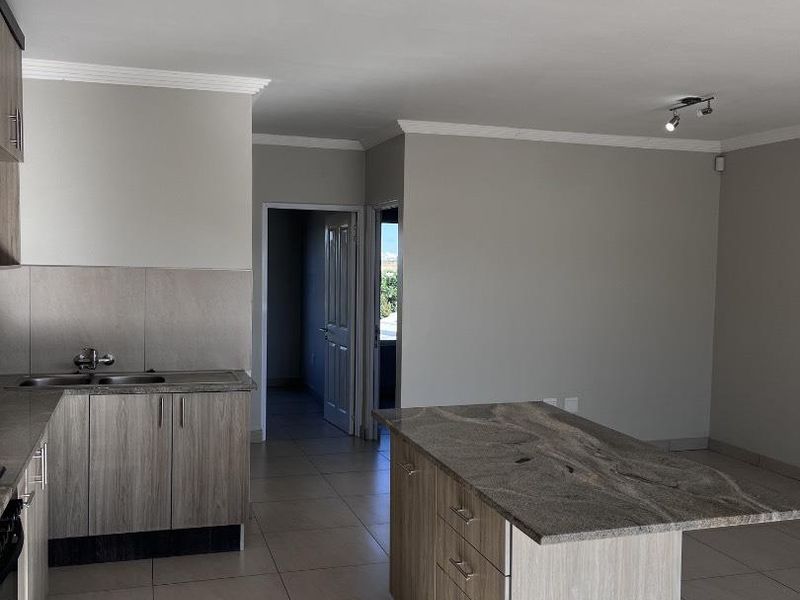 Open-plan kitchen area featuring modern wood-finish cabinetry, a granite-topped island, and neutral tiled flooring, offering a clean and functional space.