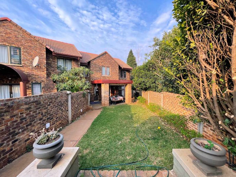 A rear view of a face brick townhouse featuring a private garden, lawn, paved walkway, and a covered patio area.