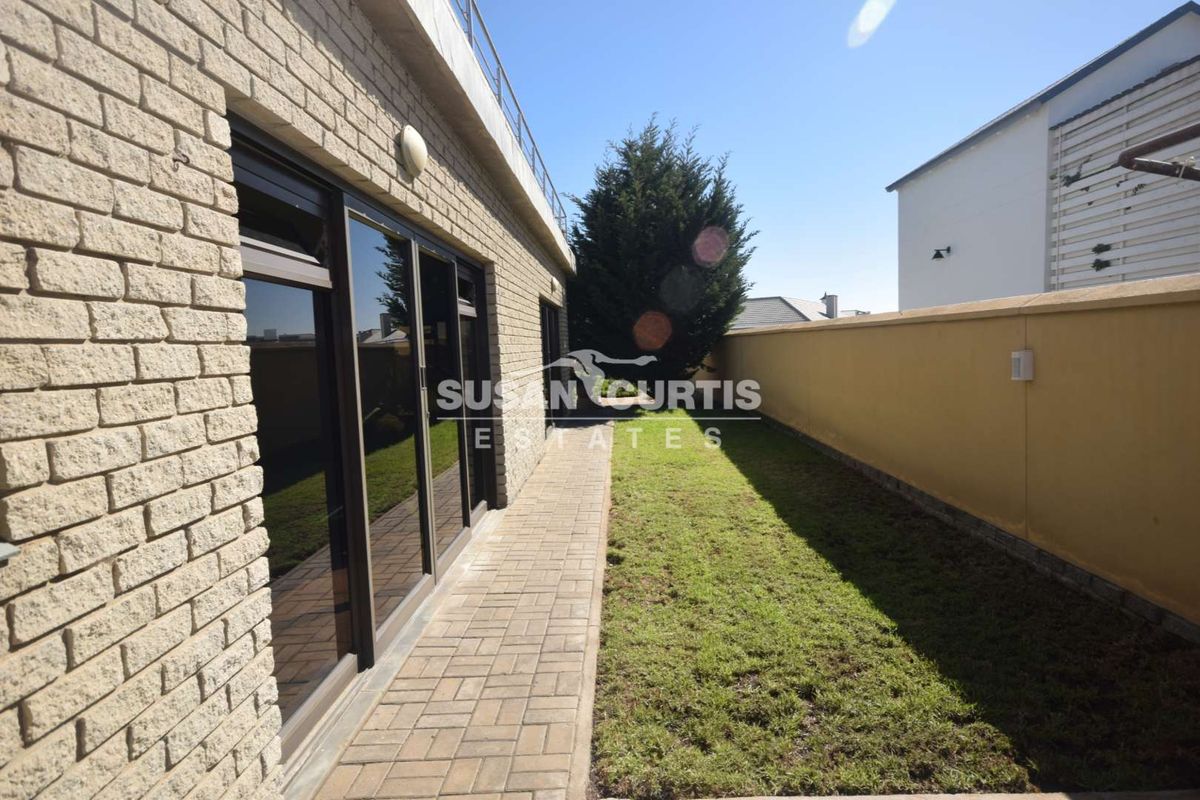 A side garden area featuring a paved walkway, brick exterior wall, and sliding glass doors leading into the property.