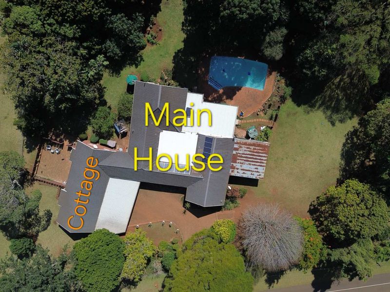 Aerial view of the property featuring a main house with solar panels, a separate cottage, a swimming pool, and extensive surrounding gardens.