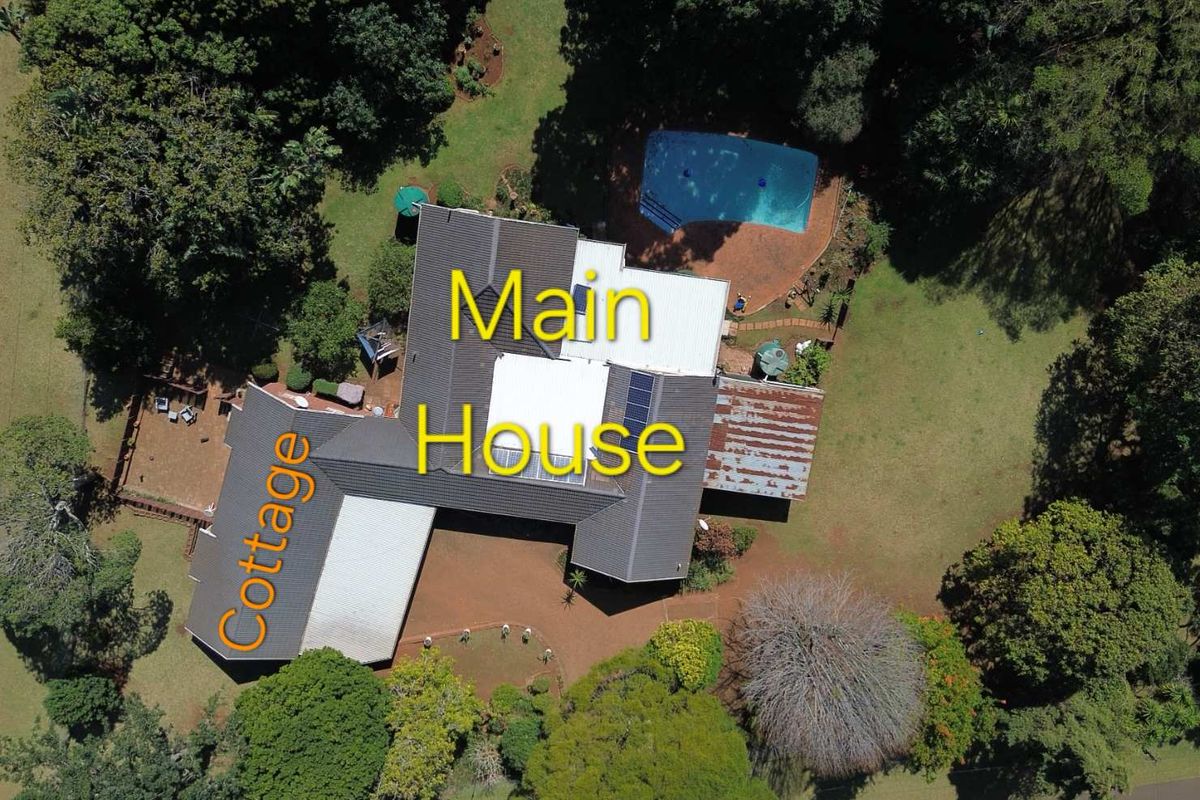 Aerial view of the property featuring a main house with solar panels, a separate cottage, a swimming pool, and extensive surrounding gardens.