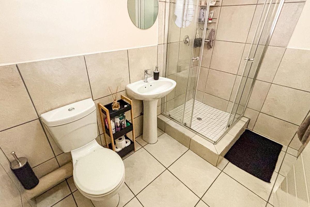 A functional bathroom featuring a pedestal basin, a glass-enclosed shower, and neutral ceramic tiling throughout.