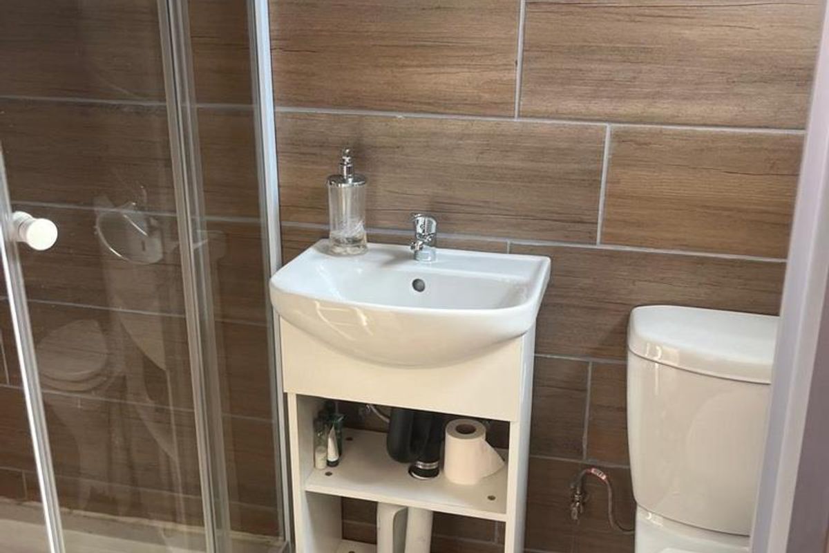 Compact bathroom featuring a glass shower enclosure, a wall-mounted toilet, and a small vanity basin with wood-look tiled walls.