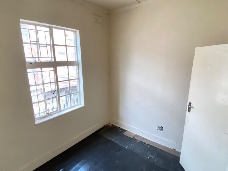 An empty bedroom featuring a window with security bars and unfinished flooring, requiring renovation to restore the space.