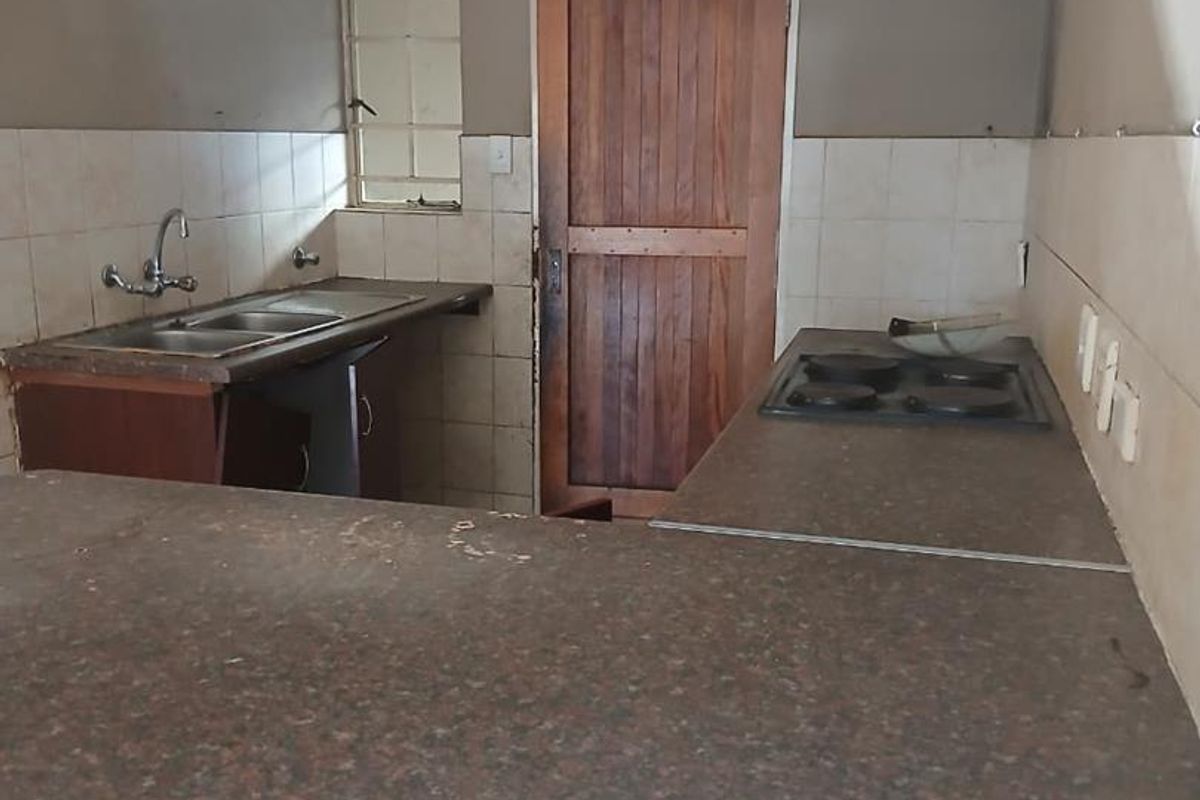A dated kitchen featuring laminate countertops, a built-in hob, double sink, and tiled backsplash, offering a functional layout ready for modernization.