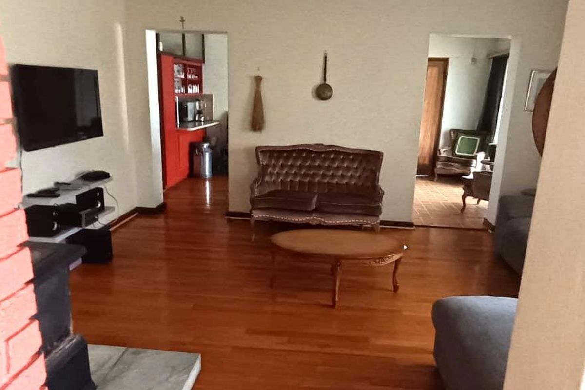 A living room featuring hardwood flooring and a prominent brick fireplace, with an open transition leading into an adjacent kitchen area.