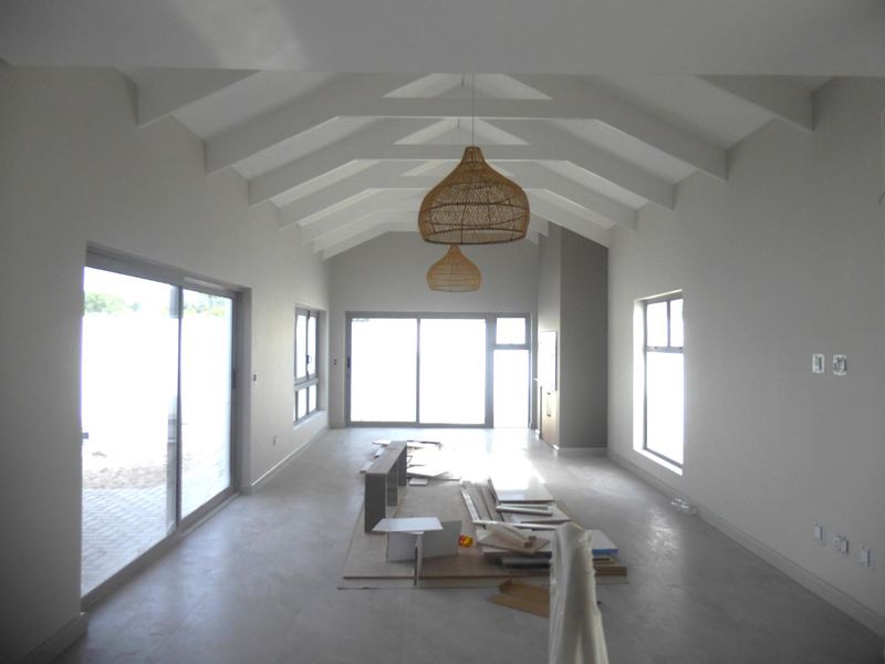 Spacious living area featuring a high vaulted ceiling with exposed rafters, concrete flooring, and large sliding glass doors providing ample natural light.