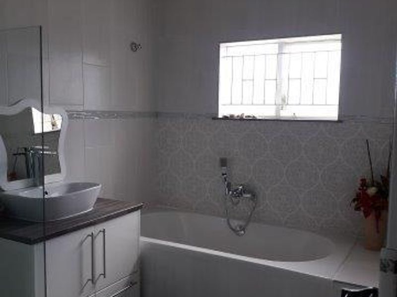 A modern bathroom featuring a white vanity with a vessel sink, a bathtub with a handheld shower attachment, and decorative wall tiling.
