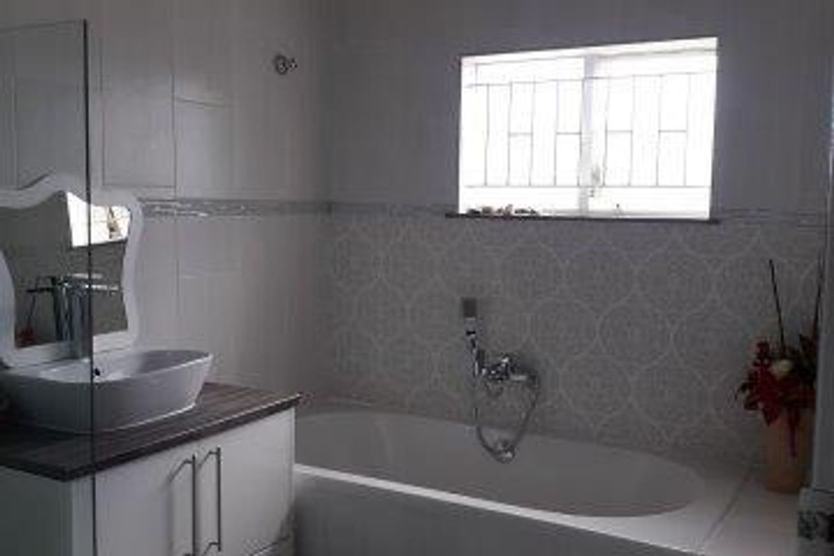 A modern bathroom featuring a white vanity with a vessel sink, a bathtub with a handheld shower attachment, and decorative wall tiling.