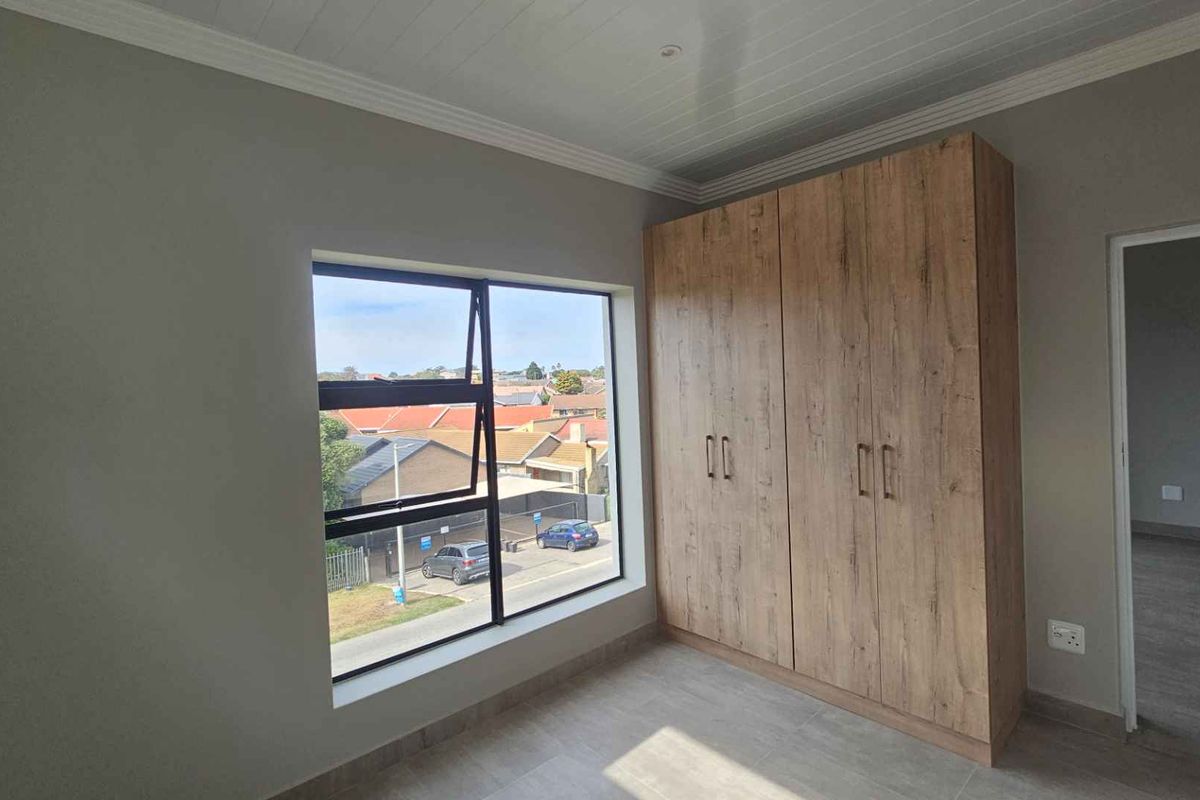 A bright bedroom featuring modern wood-finish built-in cupboards, tiled flooring, and a large window with views of the surrounding neighborhood.