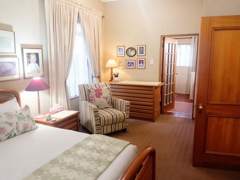 A well-maintained bedroom featuring carpeted flooring, classic timber doors, and access to an adjoining room through a glass-paneled door.