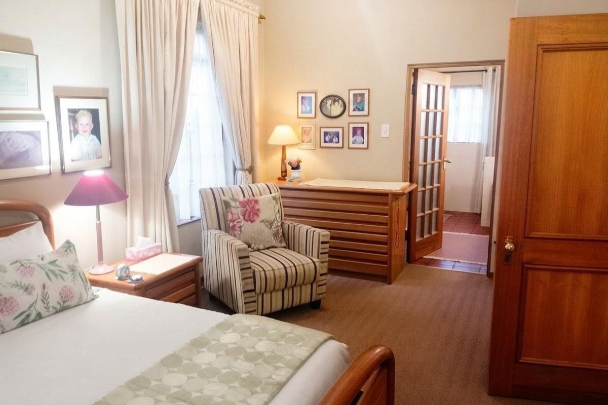 A well-maintained bedroom featuring carpeted flooring, classic timber doors, and access to an adjoining room through a glass-paneled door.