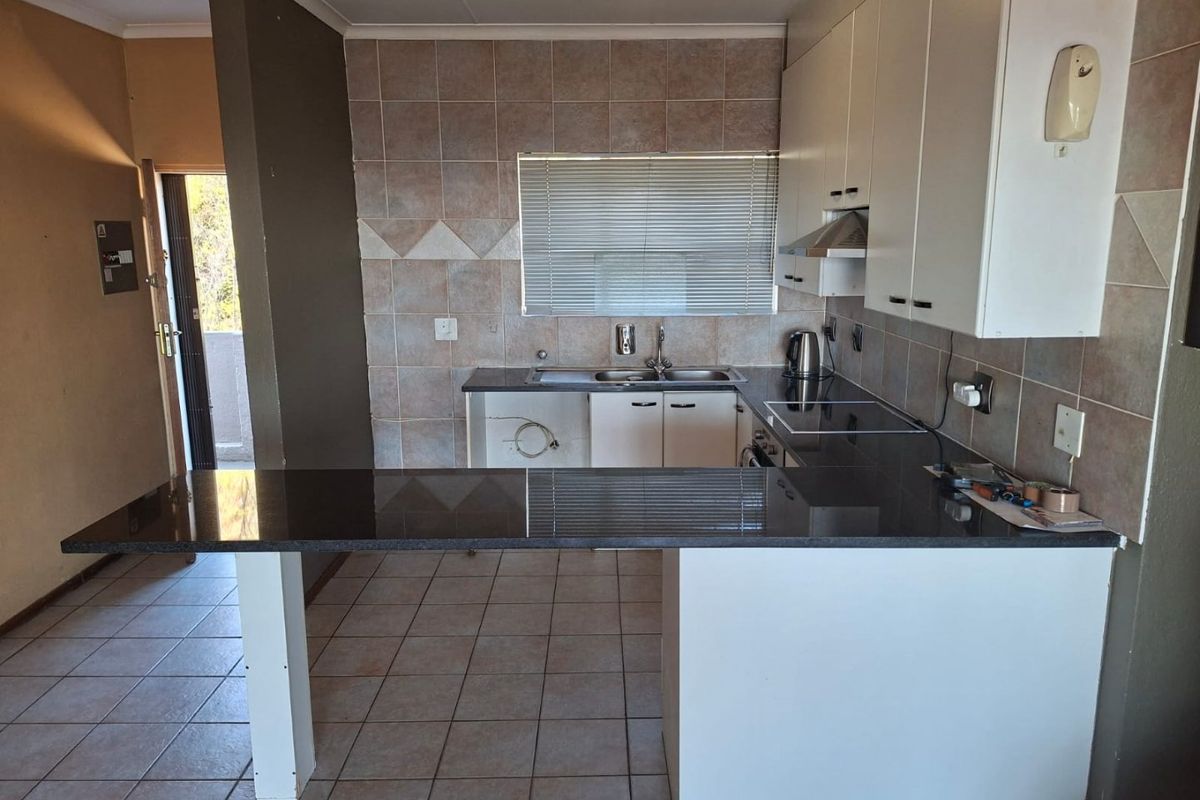 A functional kitchen featuring granite countertops, tiled backsplash, and built-in cabinetry, with an open-plan breakfast bar area.
