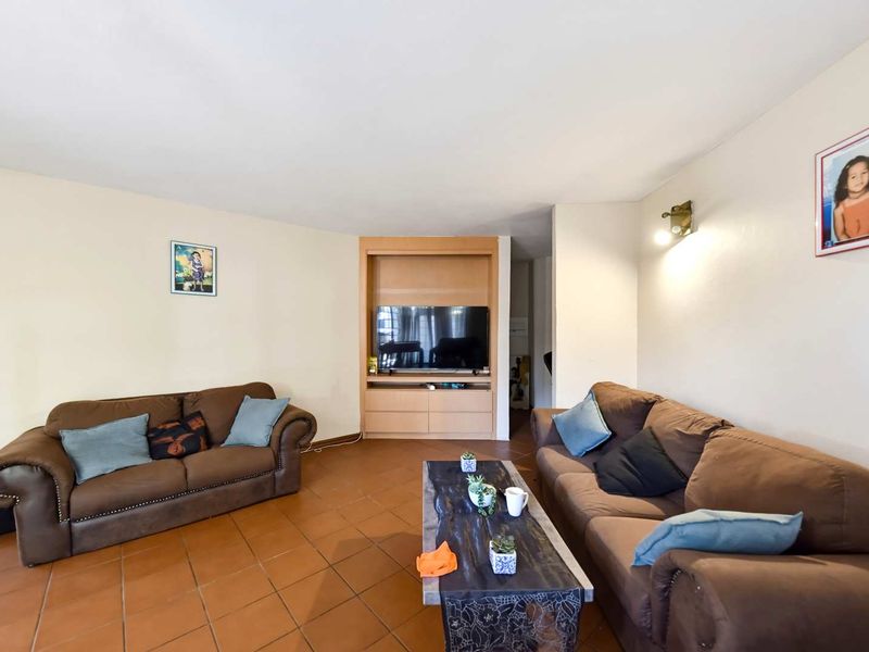 A comfortable living room featuring terracotta floor tiles, a built-in media cabinet, and warm wall lighting.