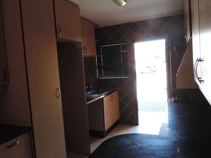 A functional kitchen featuring laminate cabinetry, dark countertops, and tiled splashbacks, with direct access to the exterior.