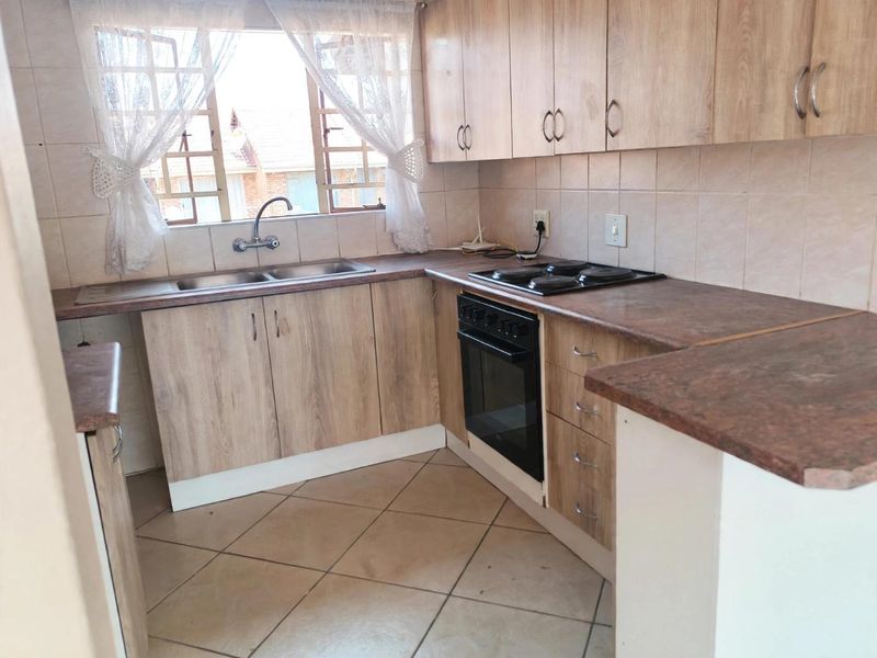 Functional kitchen featuring wood-look laminate cabinetry, tiled backsplash, double basin sink, and built-in oven with electric hob.
