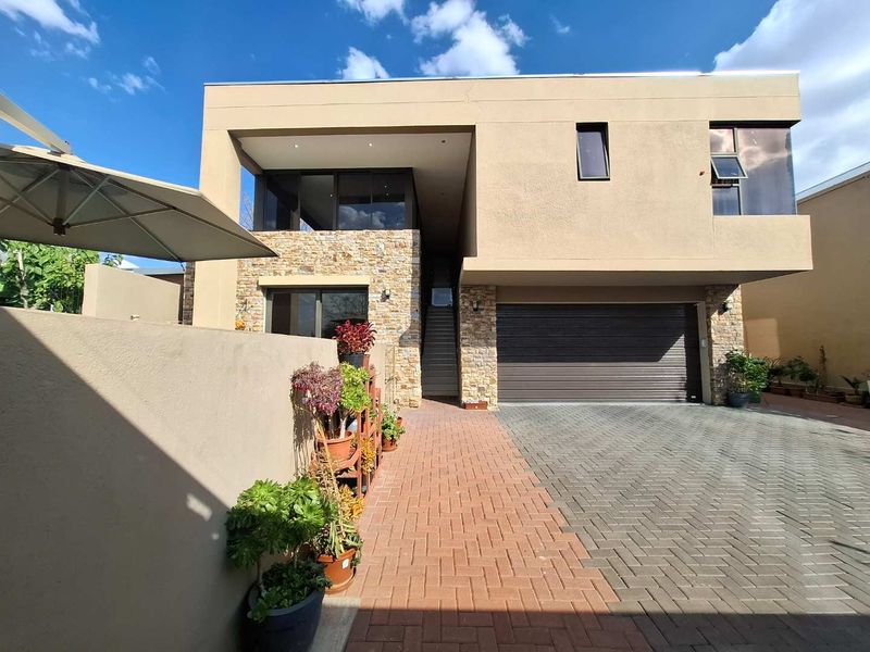 Modern double-story residence featuring stone cladding, a paved driveway, and a double garage with a recessed entrance and staircase.