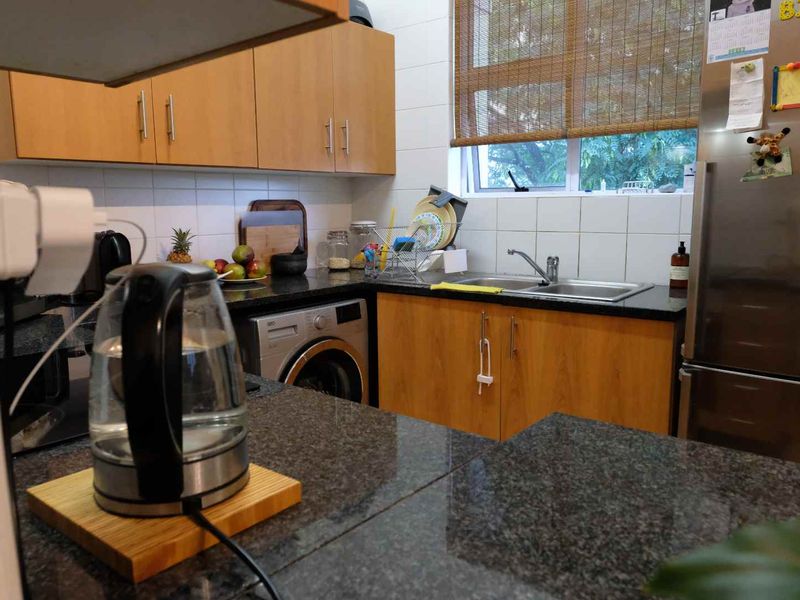A functional kitchen featuring wood-finish cabinetry, granite countertops, a stainless steel sink, and a built-in washing machine.