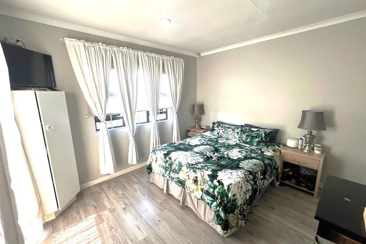 A well-lit bedroom featuring light-toned wood-look flooring, neutral wall finishes, and large windows with curtain treatments.