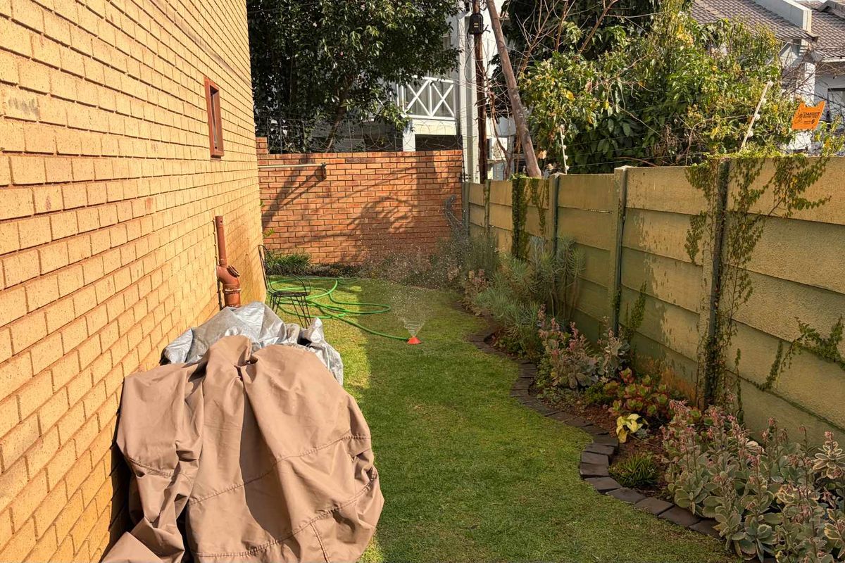 A side garden area featuring a brick exterior wall, a precast concrete boundary wall, and a well-maintained lawn with landscaped garden beds.