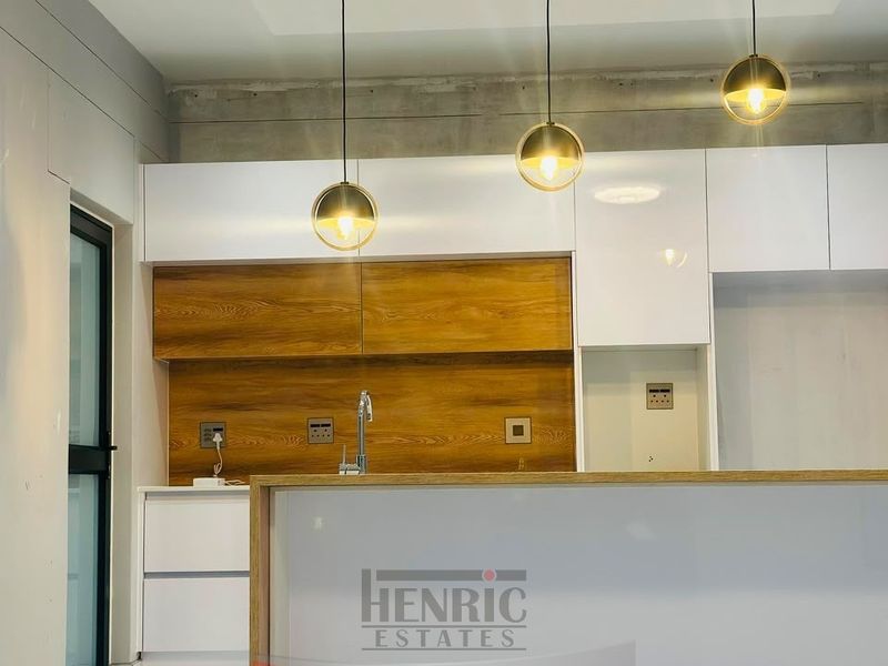 Modern kitchen area featuring white and wood-grain cabinetry, a sleek sink, and contemporary pendant lighting, currently in an unfinished state.