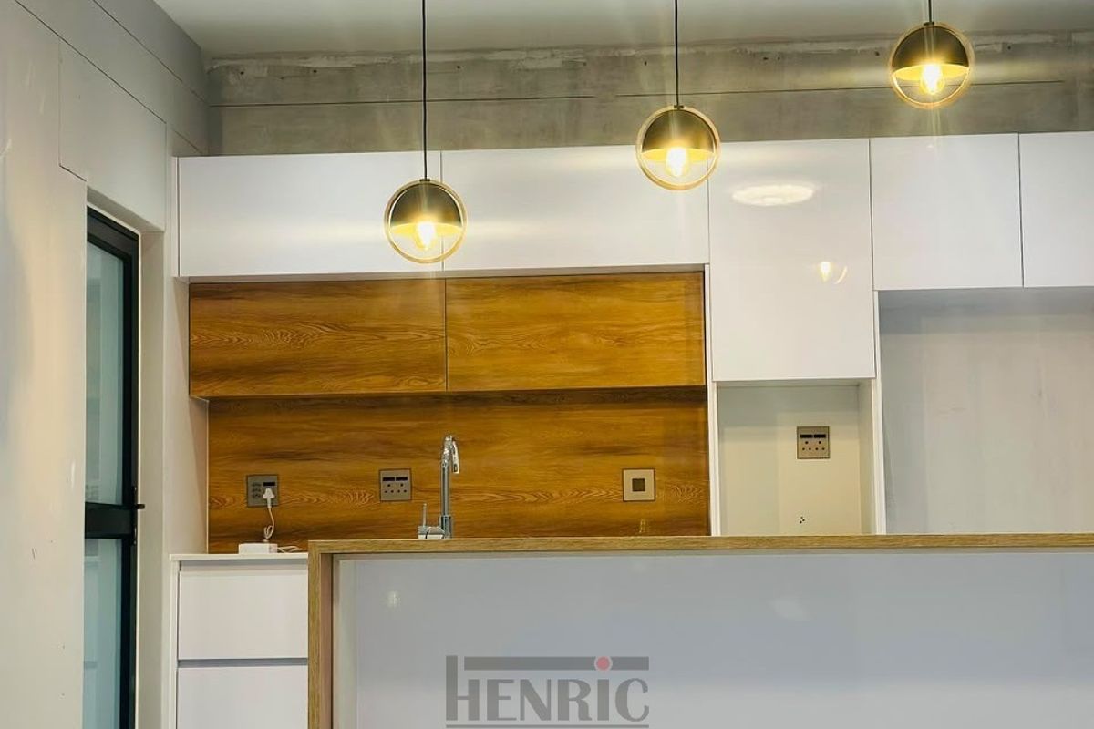 Modern kitchen area featuring white and wood-grain cabinetry, a sleek sink, and contemporary pendant lighting, currently in an unfinished state.