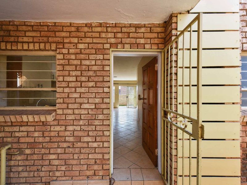 Entrance area featuring exposed brickwork, a security gate, and a timber door leading into the tiled interior living space.