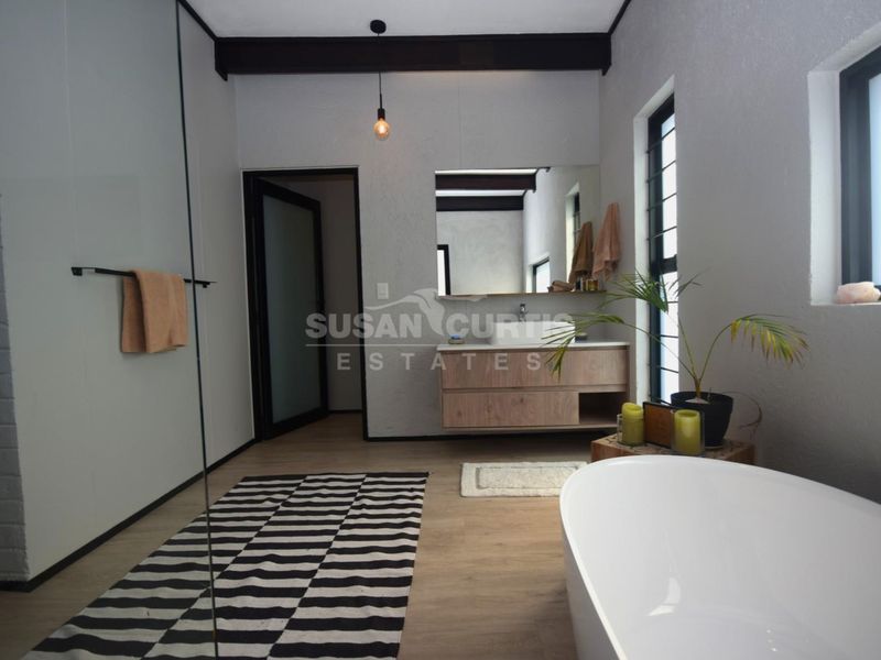 Modern bathroom featuring a freestanding bathtub, floating vanity with vessel sink, glass shower screen, and exposed ceiling beams.