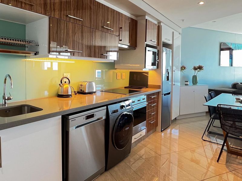 Modern open-plan kitchen featuring high-gloss cabinetry, stone countertops, integrated appliances, and sleek tiled flooring, seamlessly flowing into the adjacent living and dining area.