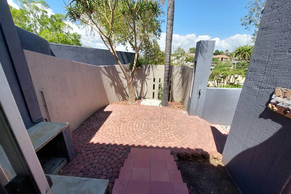 A private rear courtyard featuring a paved circular patio area, built-in masonry braai, and established garden elements.